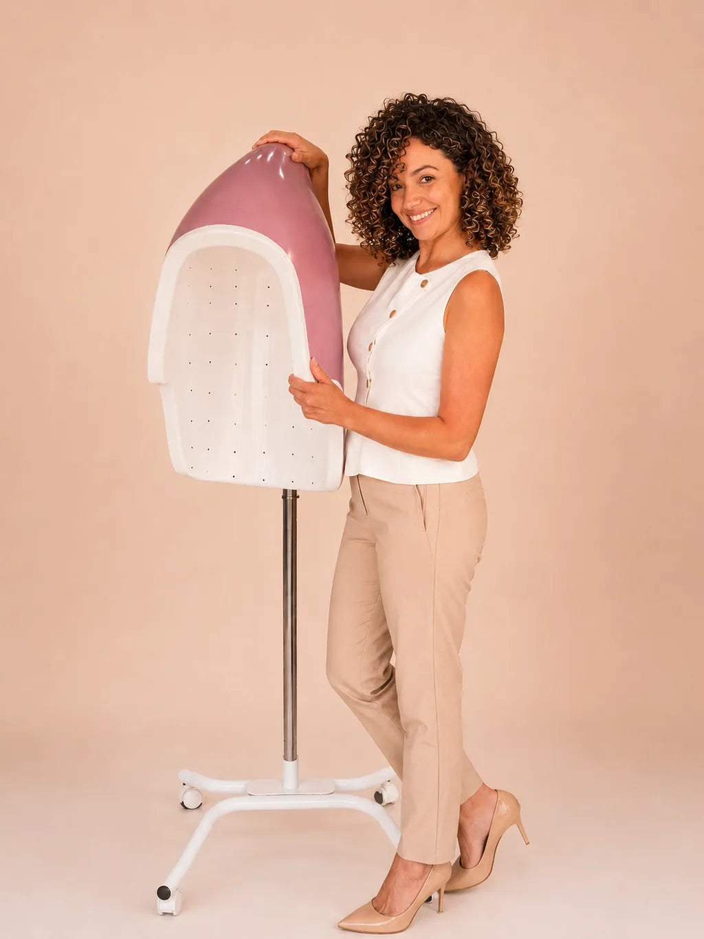 A woman standing beside a floor-standing pink Aries Air 360 diffuser, one hand resting on its open dome.